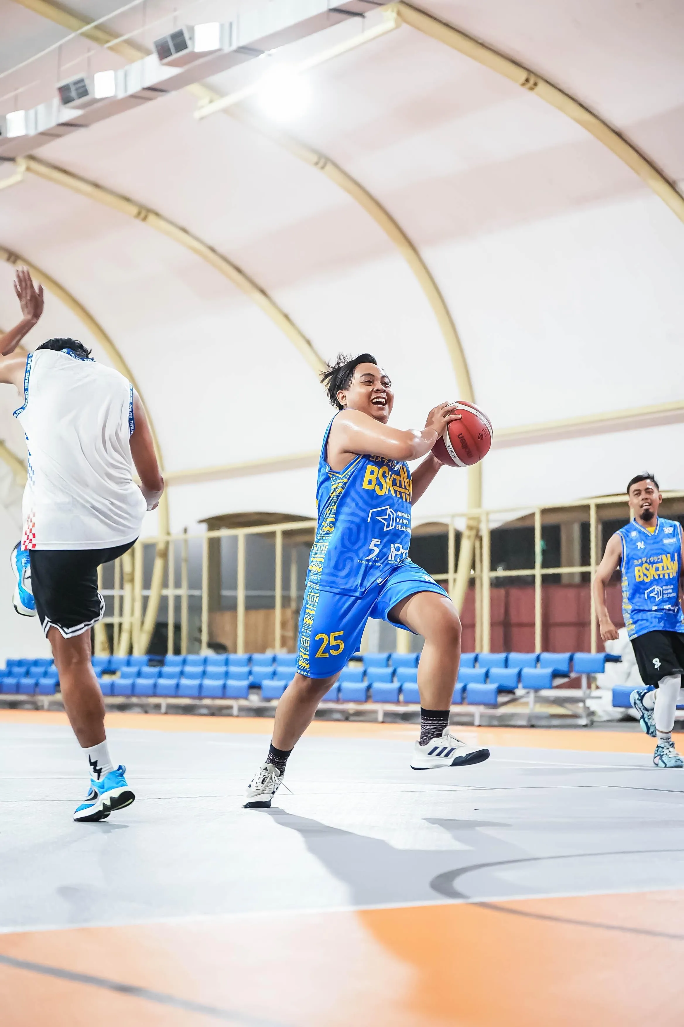 Pemain basket berkit NOIR biru menggiring bola menuju ring.