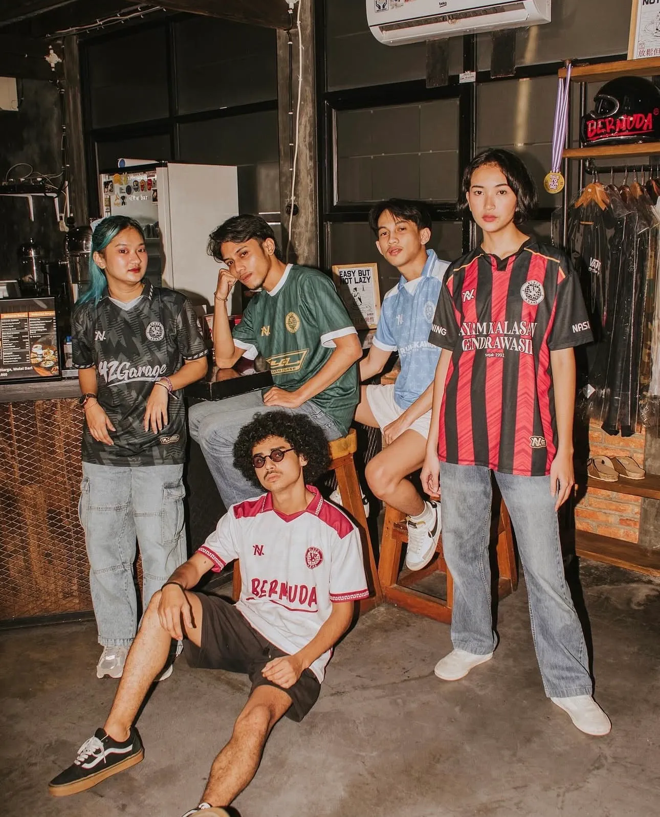 Lima orang berjersey NOIR dengan pakaian sehari-hari, berkumpul di dalam kafe.