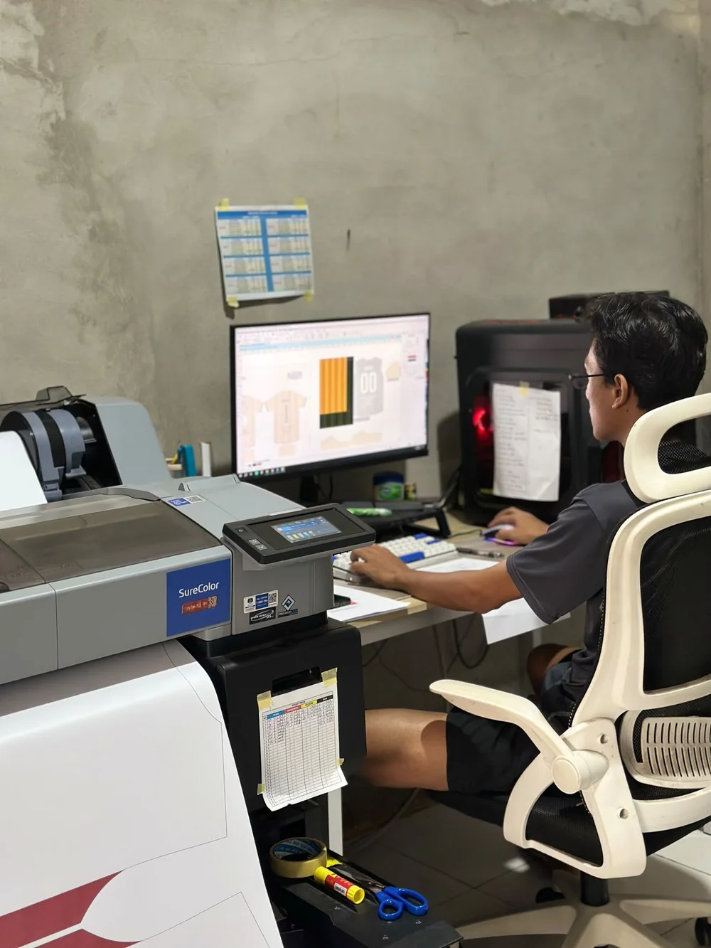 Anggota tim NOIR menata desain kit di komputer, di samping printer format besar