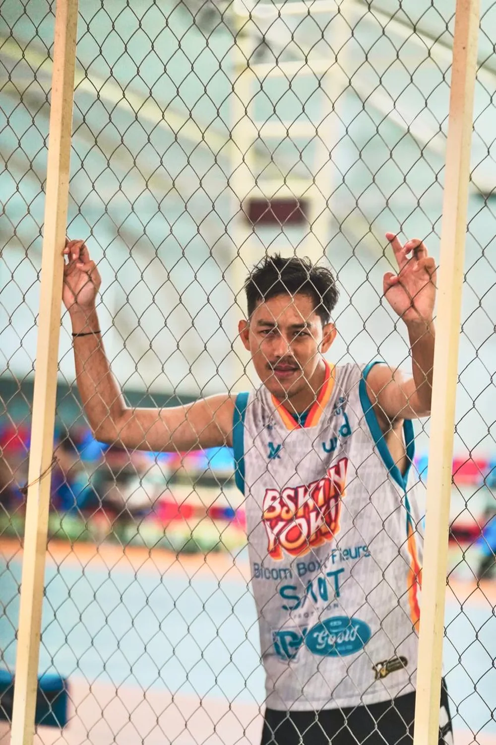 Pemain basket berjersey putih NOIR berdiri di balik pagar kawat dalam gedung